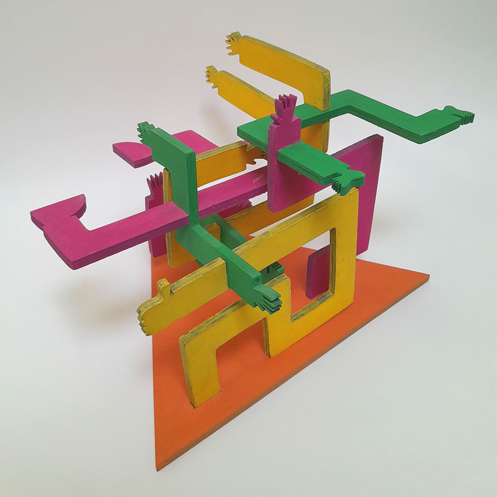 wooden 3D sculpture over white background, limb-shapes of purple, yellow and green pertrude an orange triangular base and extend beyond it.